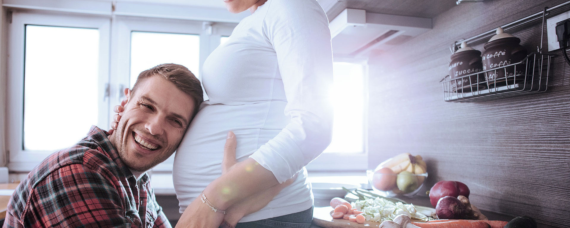 Mann legt sein Ohr auf den Bauch seiner schwangeren Frau