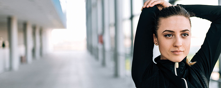 Sport Junge Frau macht Dehnübung. Sie hält ihre Arme über dem Kopf.