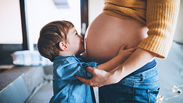 Ein kleiner Junge gibt seiner schwangeren Mama einen Kuss auf den Bauch.