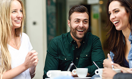 Zwei junge Frauen und ein Mann sitzen in einem Café