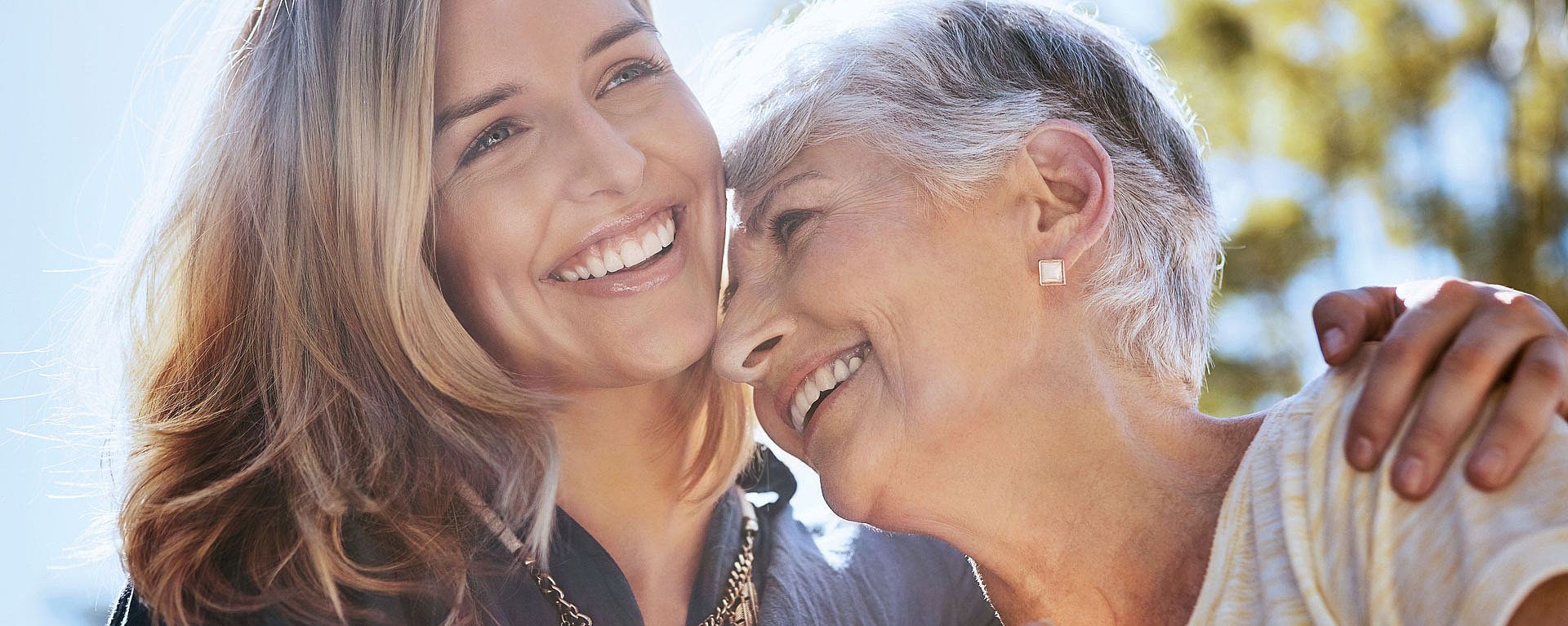 Eine junge Frau hält eine ältere Dame im Arm. Beide lachen herzlich.