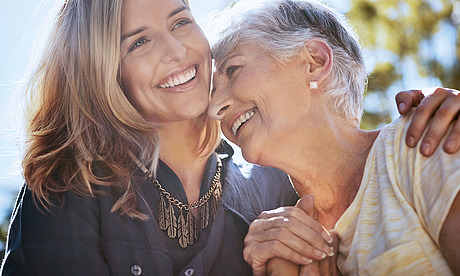 Eine junge Frau hält eine ältere Dame im Arm. Beide lachen herzlich.