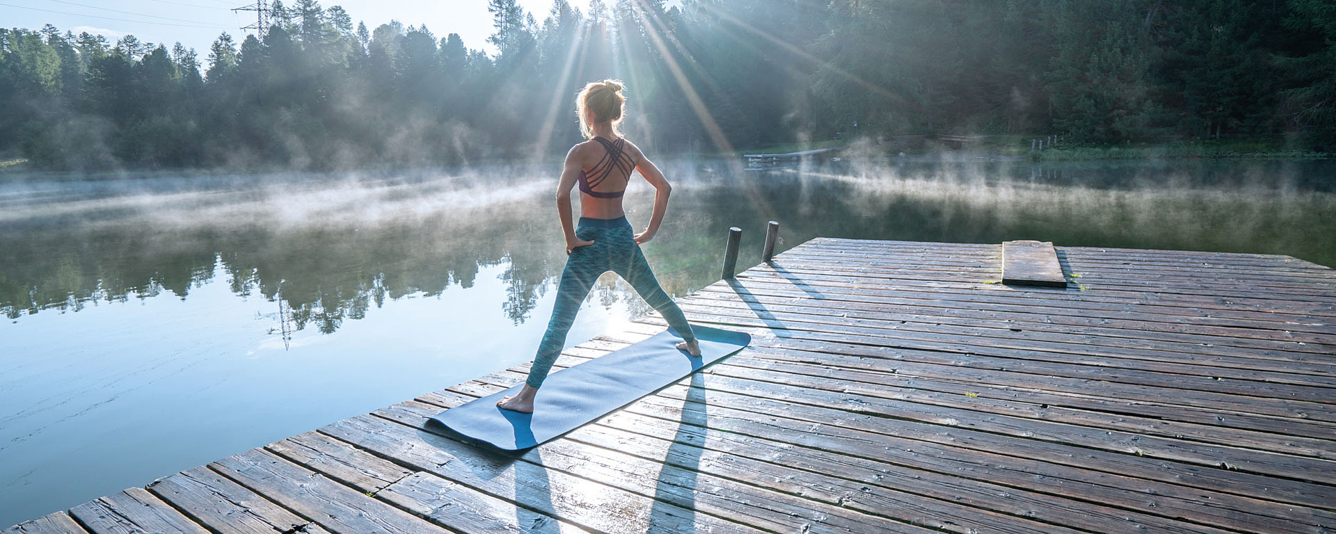 Junge Frau steht auf einem Steg am See und macht Sport-Übungen