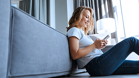 Frau benutzt Smartphone sitzend auf dem Sofa.