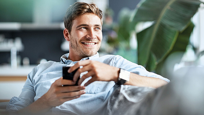 Junger Mann sitzt auf dem Sofa und hält eine Tasse in der Hand