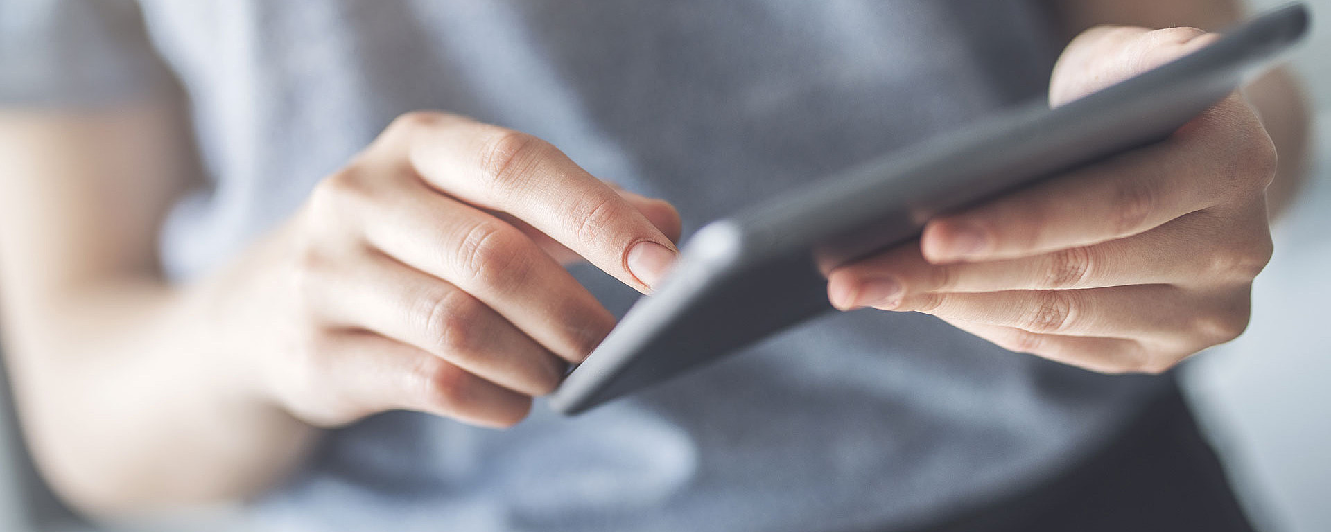 Junger Mann arbeitet auf einem Tablet. Vor ihm liegt ein Smartphone auf dem Tisch.