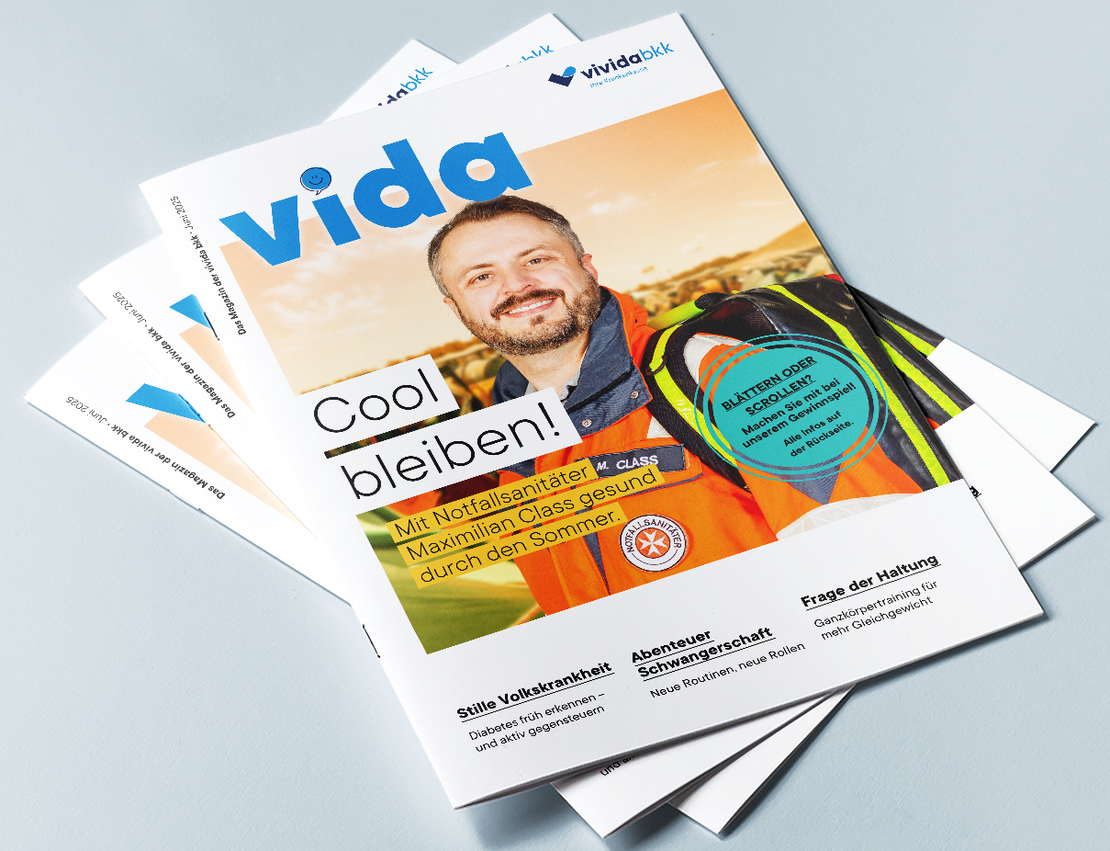 Auf einer hellblauen Fläche liegt ein Stapel „Vida“-Magazine, auf dem oberen Cover ist ein lächelnder Mann in einer Warnweste zu sehen, mit der Überschrift „Cool bleiben!“ und einem Text zur Sommersicherheit für Arbeitnehmer.