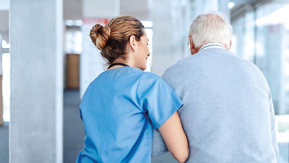 Eine Pflegerin stützt einen älteren Mann beim Gehen