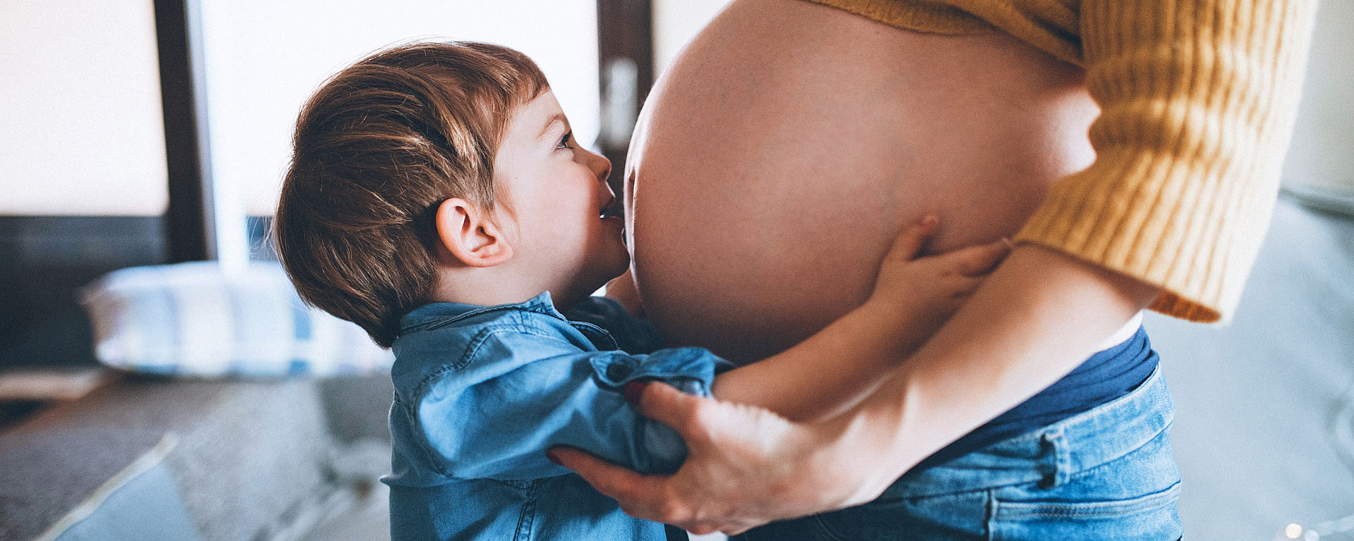 Ein kleiner Junge gibt seiner schwangeren Mama einen Kuss auf den Bauch.