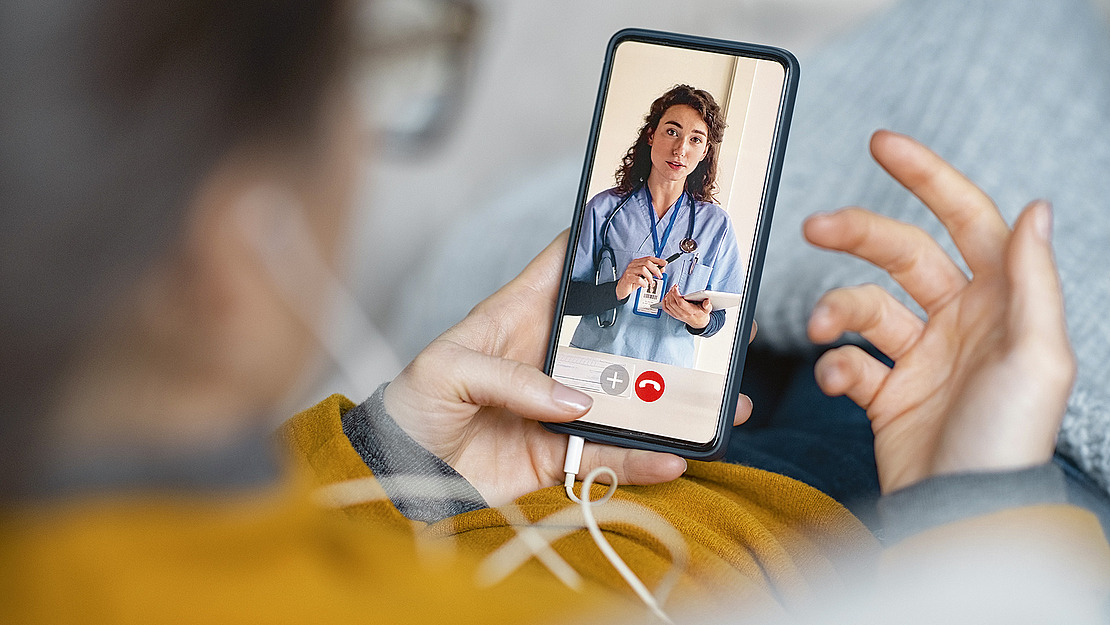 Person schaut auf Smartphone mit Ärztin auf dem Display