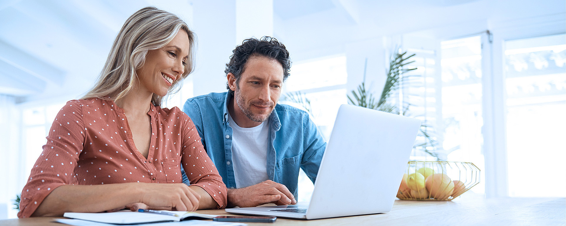 Pärchen sitzt am Esstisch und schaut gemeinsam in einen Laptop