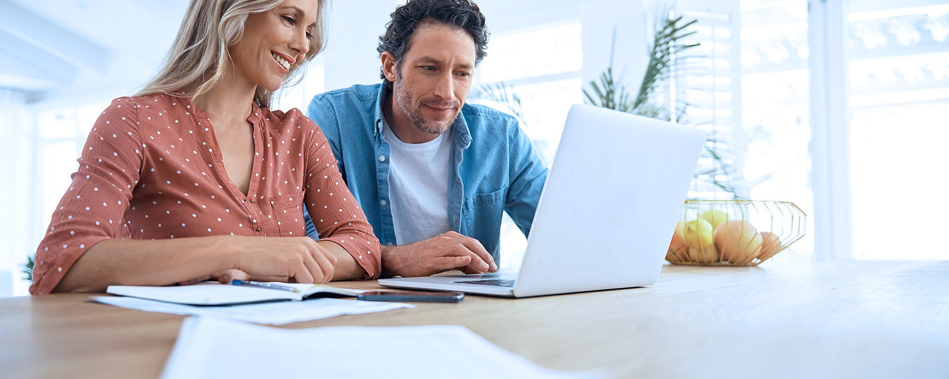 Pärchen sitzt am Esstisch und schaut gemeinsam in einen Laptop