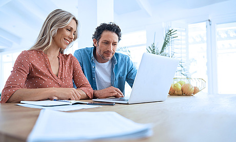 Pärchen sitzt am Esstisch und schaut gemeinsam in einen Laptop