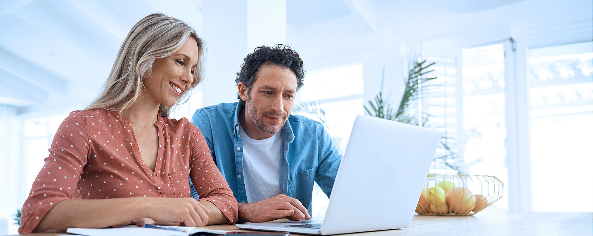 Pärchen sitzt am Esstisch und schaut gemeinsam in einen Laptop